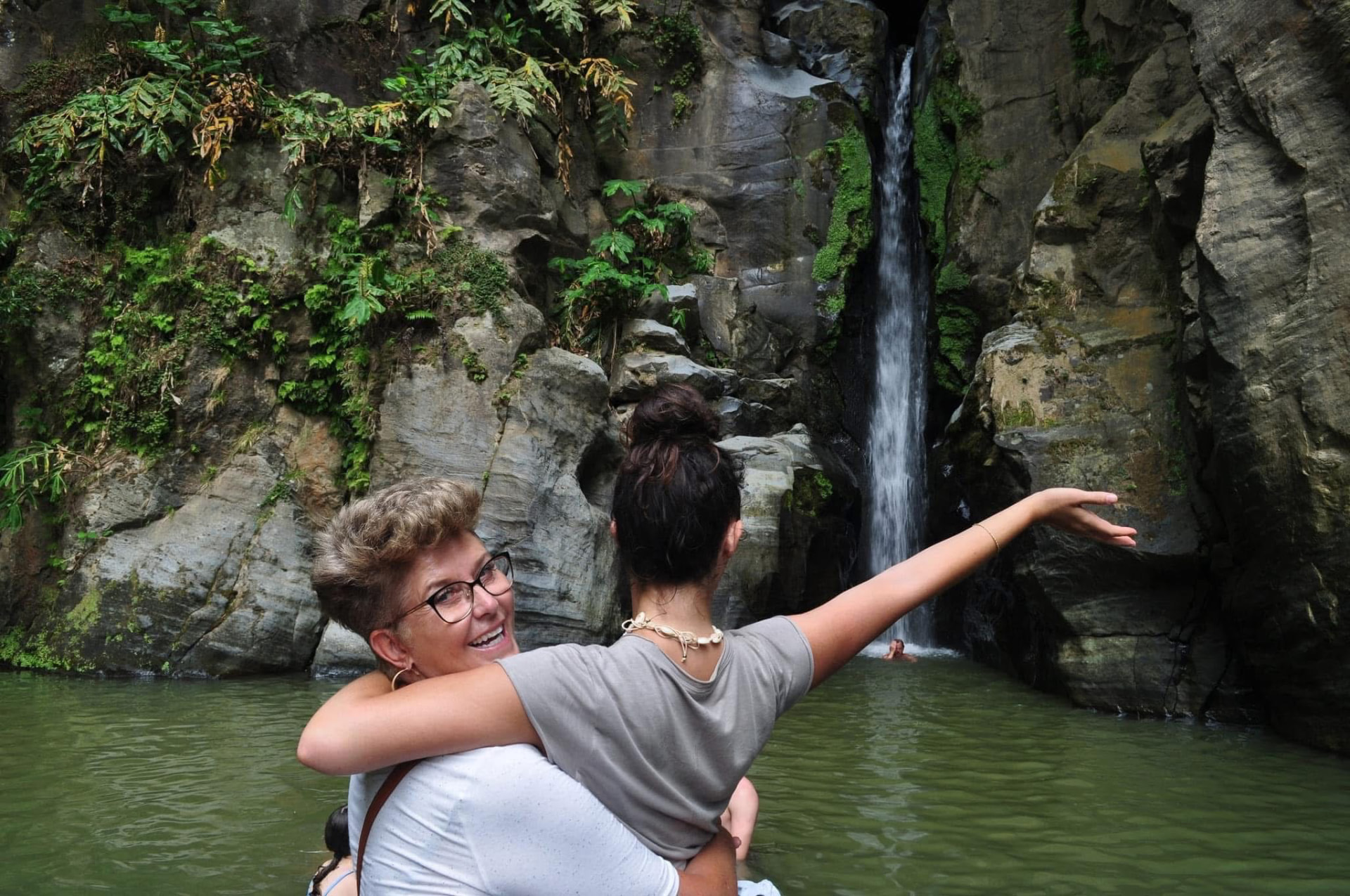 Annalyse hugging her mom in a green pool with a waterfall behind them