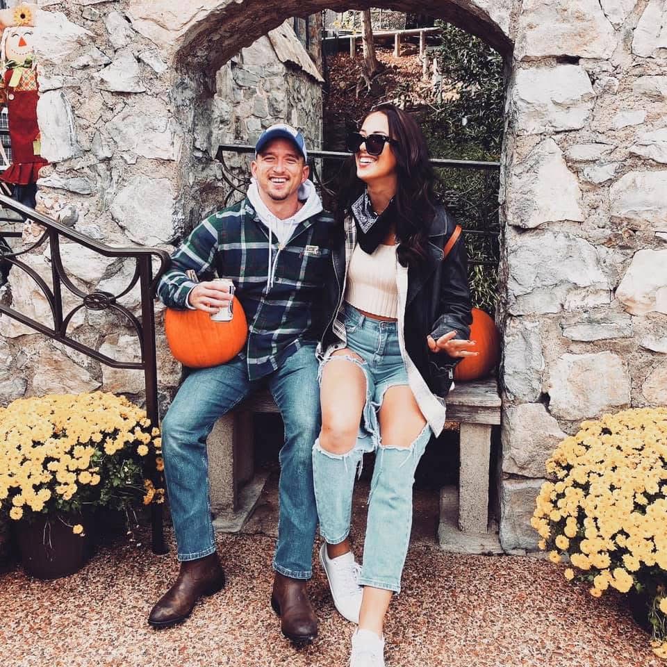 Leon and Annalyse laughing on a stone bench between pumpkins and yellow mums