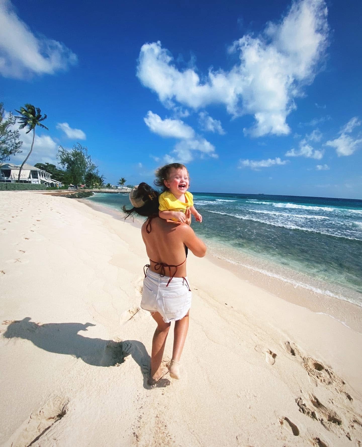Annalyse laughing as she lifts her son in the air on a bright beach